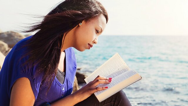 11260 woman reading bible in purple shirt by ocean